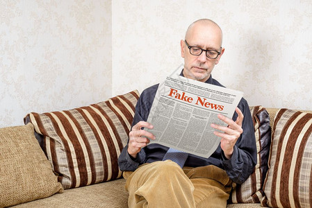 新闻纸一名戴眼镜的男人坐在家里沙发上看报纸导假新闻冒消息LoremImpsum文本出版打印图片