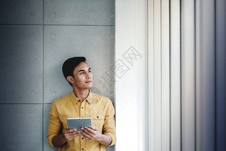 利用数字平板看远路和微笑梦想取得成功办公室的窗口站立着快乐商人的肖像现代工作积极图片