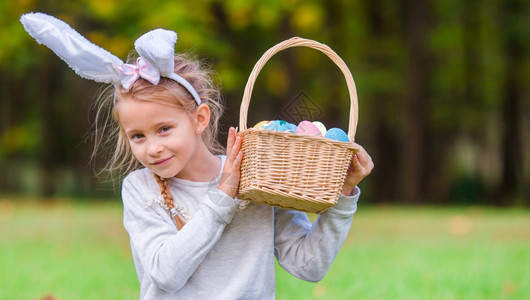 穿着兔子耳朵和复活节鸡蛋篮子的可爱女孩在复活节时子户外吃鸡蛋的肖像美丽乐趣草地图片