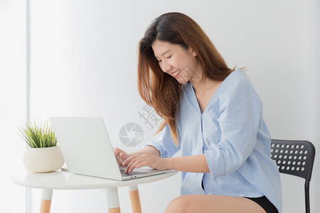 随意的自信坐在家中工作时使用笔记本电脑的亚洲女年轻美丽亚洲女在家打字时笑容在线的图片