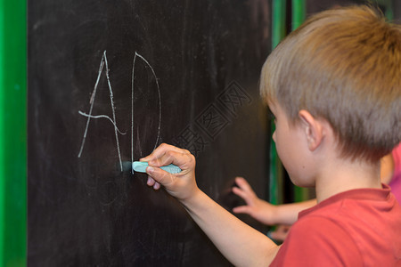 美丽的小男孩学会在幼儿园或教室的黑板上写字小男孩学校白色的图片