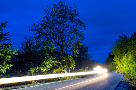 交通晚上夏夜森林中一条空路的灯头照亮长风车道夜路和朝车辉光图片