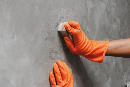 戴橙色橡皮手套的人用来转换混凝土墙上的洗涤剂干净打扫瓷砖图片