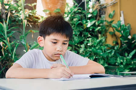 亚洲男孩用笔写书做功课的亚洲男孩可爱桌子年轻图片