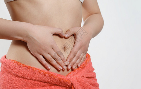 锻炼母亲一个年轻女孩在她的肚子上用白色手展示心脏象征早孕概念和女健康成人图片