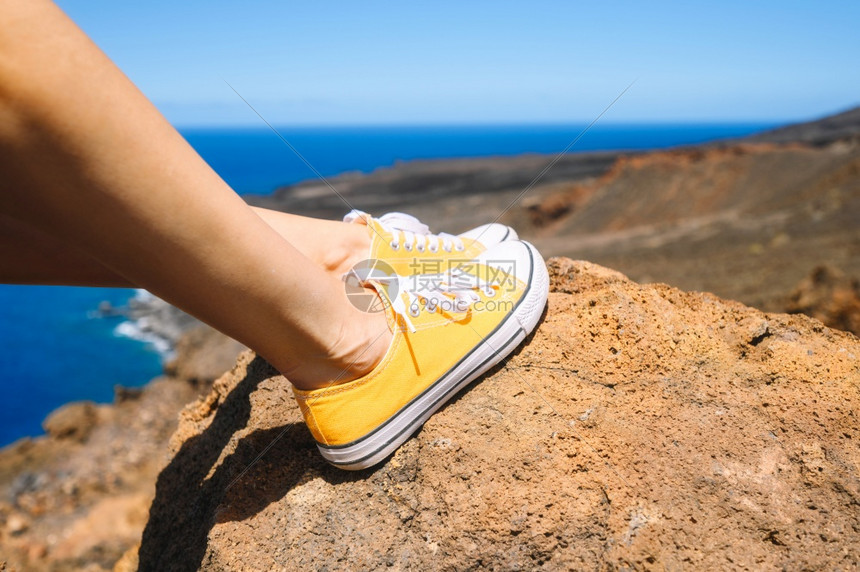 穿着黄色运动鞋在岩石上渡假紧贴高品质的相片放松享受风景旅行者坐在岩石上穿黄色运动鞋在夏天游荡中近距离她放松了享受风景旅行者坐在岩图片