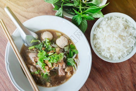 烤牛肉面条汤白碗中烧猪球和蒸饭木板茶桌上的叶泰国风格土制餐桌边面包叶食物炖热的图片