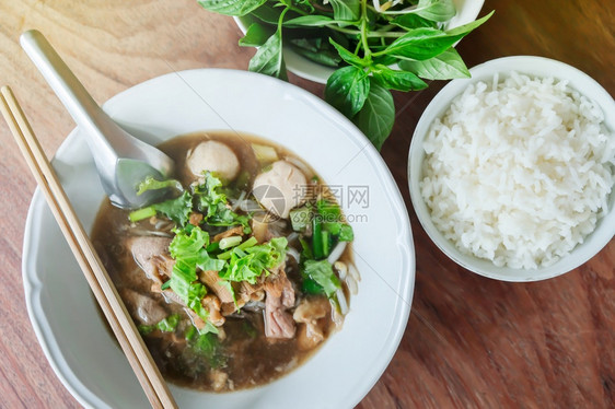 烤牛肉面条汤白碗中烧猪球和蒸饭木板茶桌上的叶泰国风格土制餐桌边面包叶食物炖热的图片