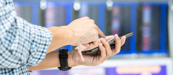 移动的旅游在机场终端飞行信息板上使用智能电话通过在机场交旅行休假和技术上的移动电话在线检查时速男旅行者假期和技术等机载手的网上检图片