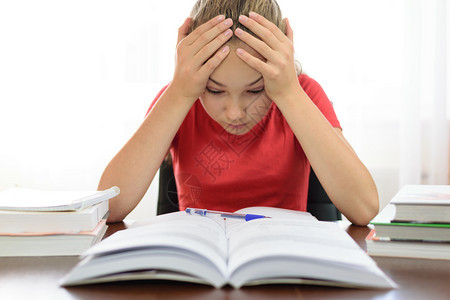 女学生将头握在桌上的一堆书架对学校功课问题感到疲倦和沮丧女孩在学校做功课的问题知识不所措沮丧的图片