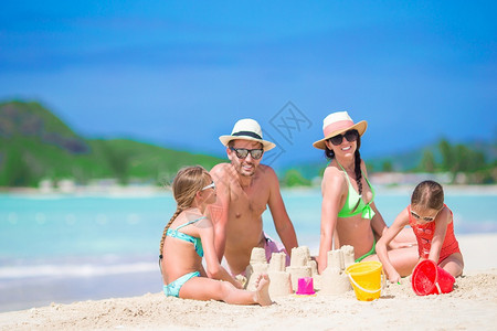 在热带海滩制作沙堡的家庭图片