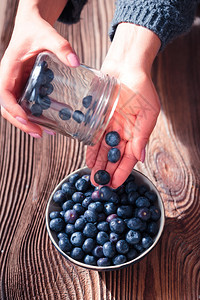 女人把刚从罐子里收集到的蓝莓放一个小碗迪许放在老木板桌子上营养收成图片