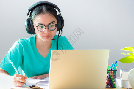 亚裔年轻女学生带眼镜耳机在笔记本电脑大学的膝上型计算机大学课程在线网上互联学习远程教育的书籍视电会议上认真研读严肃的写作说明在家图片