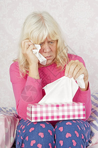 卧室灰色的带着粉红睡衣和纸巾的悲哀妇女坐在地板上躺床疼痛图片