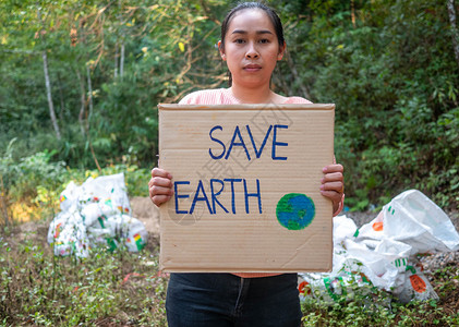 外部持有拯救地球海报的年轻女展示了抗议森林中塑料污染的征兆世界环境日零废物的概念世界环境日零废物概念WorldEnvironme图片