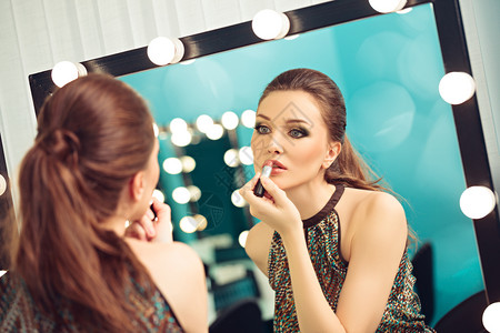 嘴唇模型青年轻女人在镜子前涂口红的图片