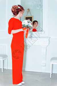 身纤细新娘精品店穿着红裙子的年轻美女穿着假日发型和一束花在镜子里看着有选择的焦点红对照镜的女人吸引们背景