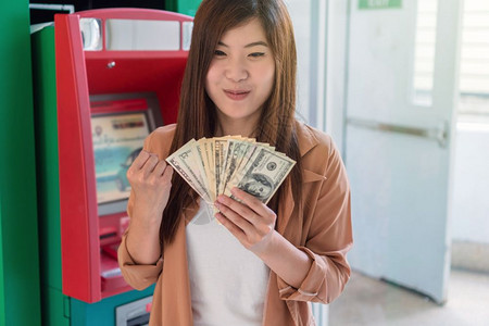 塑料借方在自动取款机提现金商业自动资转移概念后快乐的年轻女持有美元货币并微笑地行动起来银业图片