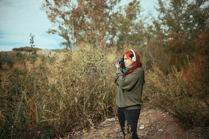 女孩积极的年轻子在森林里拍照用旧的模拟相机和耳拍摄芦苇图片