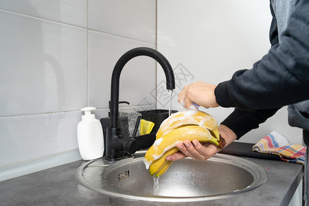 擦洗在水槽下持有香蕉的不明天主教男子手中的侧面视图在水池下用肥皂清洗结水果用中清洁肥皂消毒到厨房里家对或污染进行消新鲜的有机图片