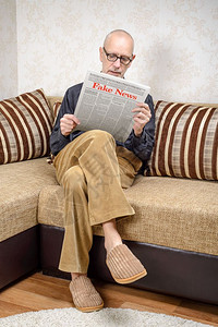 新闻业一名戴眼镜的男人坐在家里沙发上看报纸导假新闻冒消息LoremImpsum文本小报公图片