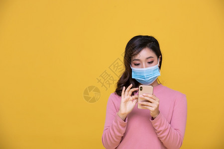 感染脸污身戴面罩或保护的亚洲美丽快乐年轻女防止冠状危机或COVID19爆发她使用手机或智能处理黄色背景情况COVID19图片