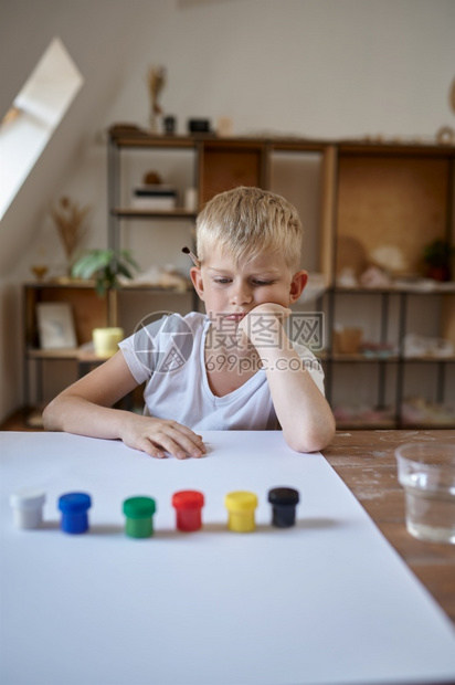 小男孩在桌边用古阿切画小男孩在艺术学校上讲课的孩子年轻画家愉快的爱好童年小男孩用古阿丘画小男孩工作间里的子艺术绘画乐趣图片