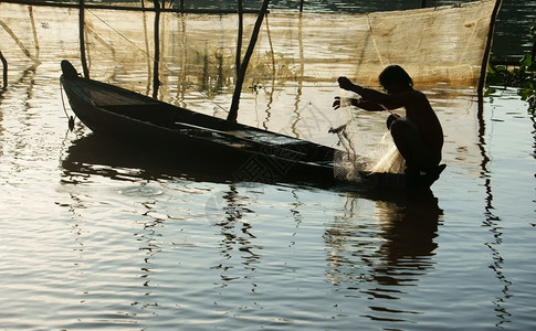 亚洲人们轮船上的渔民坐在轮船上捡网修理捕鱼作业以在洪水季节的清晨在河上捕捞鱼职的图片