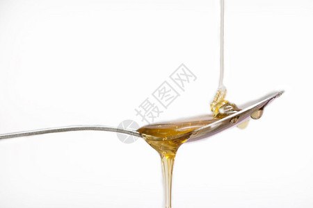浸渍生的蜜糖蜂从银勺子上滴落在孤立的白色背景食物上蜂蜜从孤立的白色背景银勺子上滴水图片