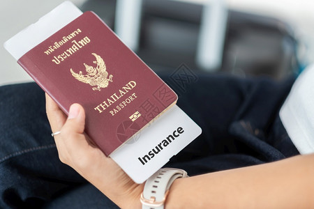 航空公司游客持有泰国护照和旅行保险文件及李袋背景的泰国妇女手持护照和旅行保险证件度假和运输概念旅行和运输文档背景图片