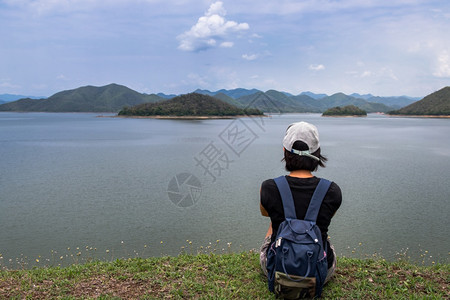 年轻的游客美丽在湖岸边坐在和享受美好景色平时刻的年轻青女背影其景为假日旅行概念休息和享受生活方式选择重点等山脉分布在上图片