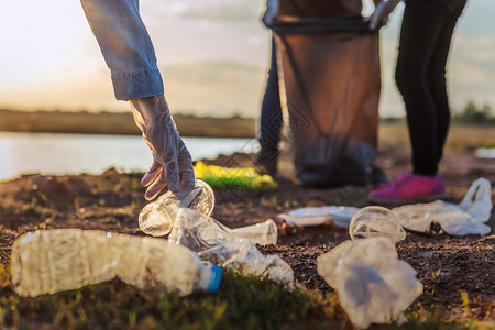 在日落时靠近河流的公园里将垃圾塑料瓶装入黑袋人类乐观的手图片