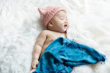 可爱的保护皮肤新生儿30天大男孩在白床上笑着微在蓝包布下放松感到快乐图片