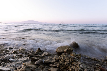 接触云美丽的日落时在希腊Zakynthos的石滩上海浪图片