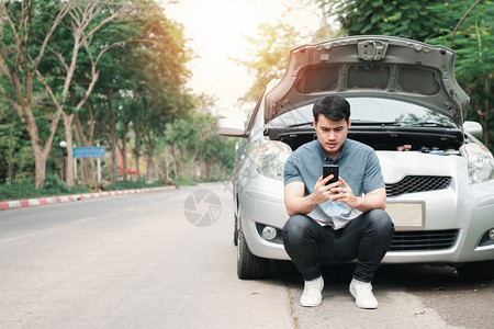 路人们使用移动电话的亚洲男子在街头汽车故障后要求援助车辆发动机问题概念或事故以及专业技工的紧急帮助在交通失灵之后使用移动电话的亚图片