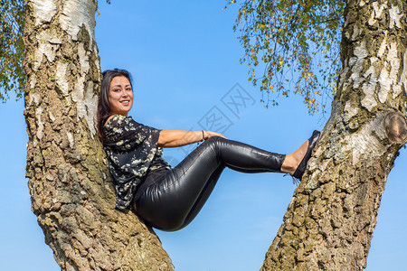 头发松弛年轻的黑人印度女坐在蓝天空的白树上裤子图片