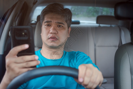 亚洲男子驾驶汽车时使用移动智能手机和阅读信息疏忽危险行为和事故风概念a过失危险行为和事故风的概念高速公路交通操舵图片