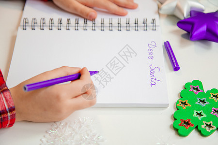 白色的孩子们亲爱圣诞老人信贺卡一个拿着笔的孩子在木制背景上的白纸写字带有新年装饰童梦想的礼物新年概念亲爱的圣诞老人信贺卡一个拿着图片