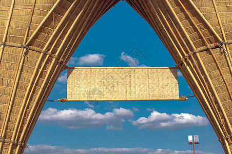广告框架悬在蓝天空和白云背景的大型竹拱门上空白竹形标志注招牌图片