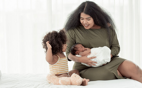 育儿兄弟姐妹非洲黑人妈在家卧室照顾自己的小儿子和女非洲黑人母亲在卧室里照顾她的儿子和小女婴图片