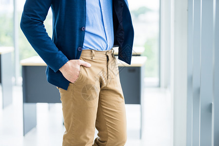 男人或者一名商Manrsquos手持棕色或金裤口袋身着蓝外套和衬衫在办公室背景中穿着蓝色夹克和衬衫在办公室背景中随意的图片