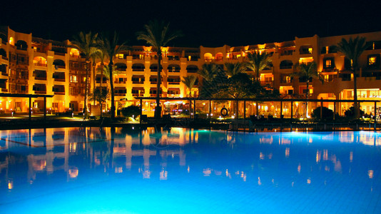 闲暇游泳池和假日晚间酒店人们上在游泳池附近放松晚间酒店的灯光在夜晚池水中反射赫尔格达度假村酒店的明亮灯光人们在游泳池附近放松暮埃图片