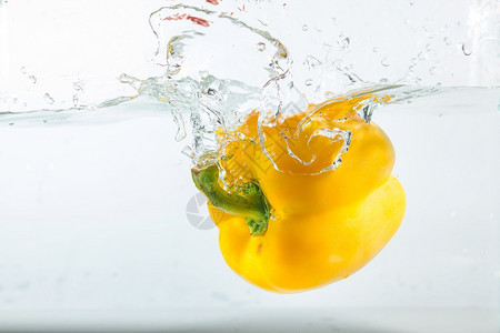 甜辣椒在水中喷洒黄色的白背景甜辣椒是一种不成熟多汁的胡图片