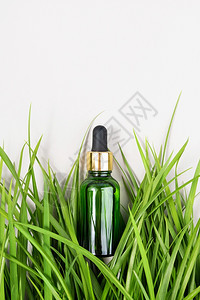 一个绿色玻璃瓶在白背景的绿草中加入血清精油胶原蛋白或其他化妆品天然有机温泉化妆品概念样机顶视图一个绿色玻璃瓶在草中加入血清胶原蛋图片