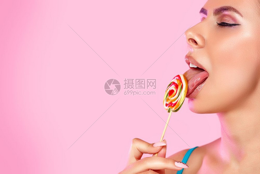 丰富多彩的一位年轻美丽女孩舔着一个多彩明亮的洛利波普Lollipopop她用的舌头在粉红色孤立的背景和复制空间上近距离拍摄焦糖吸图片