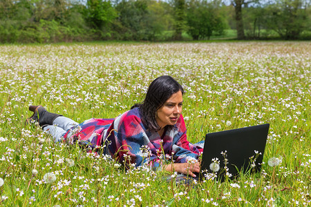 哥伦比亚妇女躺在盛开的草地上在笔记本电脑上工作学习自然接触图片