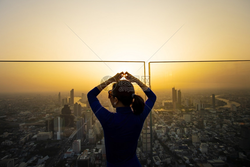 经过市中心天际线用手指站在高楼的摩天大上与日落天空的金光相对来塑造女人的心形图片