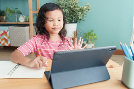 教育药片课亚洲小女孩在家庭早晨以平板数码器在室内地用平板数字打贺礼在线辅导时挥手的亚洲小女孩在家网上学习概念图片