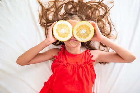 化妆品小姑娘对躺在床上的柑橘柠檬玩得开心小姑娘用柠檬半径遮住眼睛肉欲幸福图片