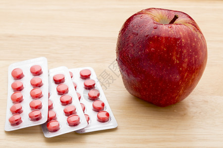 棕色的疾病健康红药丸泡罩包装和红苹果色药丸泡罩包装和木背景上的红苹果图片